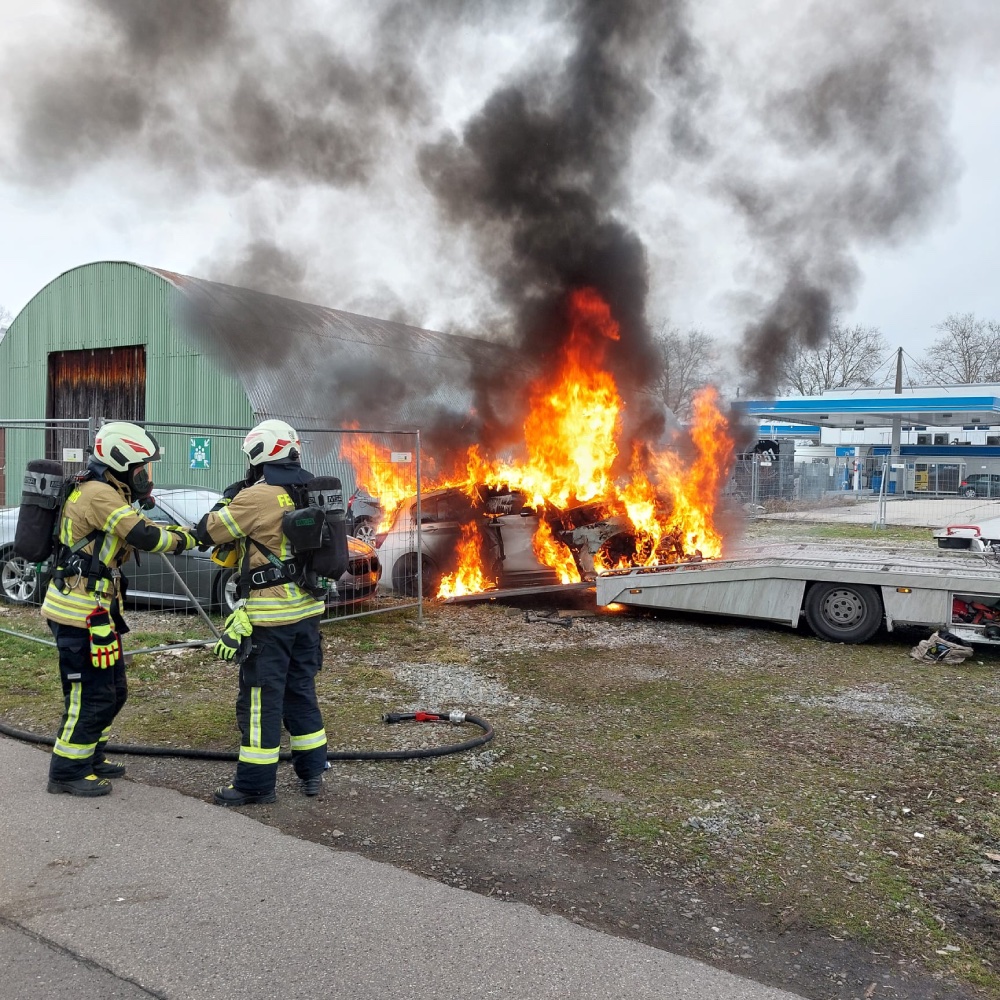 Zwei Feuerwehrleute löschen ein brennendes Auto.