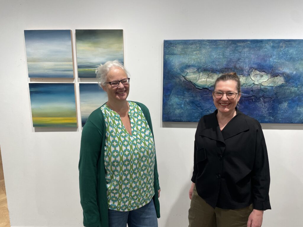 Zwei Frauen vor einer Wand, an der Kunstwerke hängen.