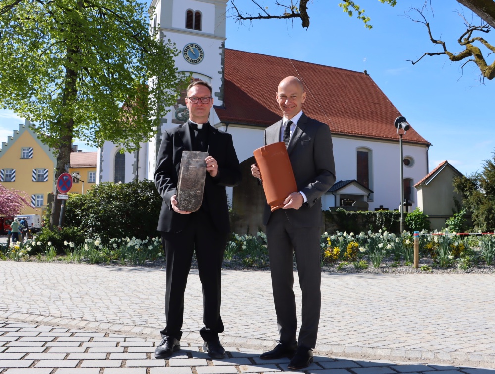 Zwei Männer stehen vor einer Kirche und halten Ziegel in der Hand.