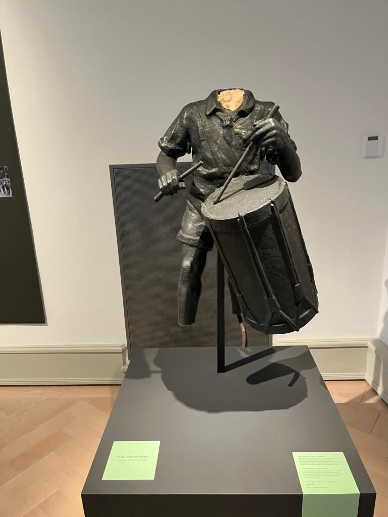 Eine Jungenstatue, ohne Kopf und Füße, der auf einer umgehängten Trommel spielt
