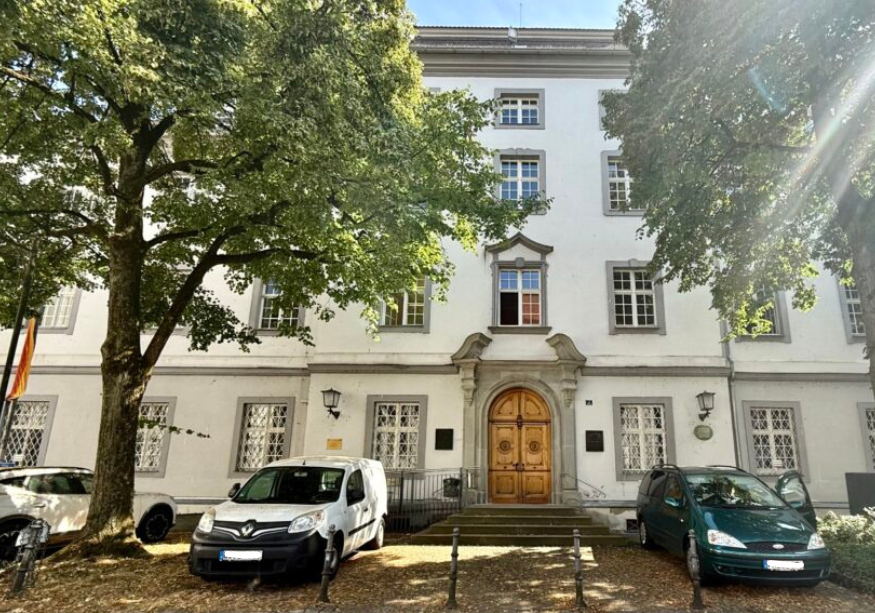 Mehrstöckiges Gerichtsgebäude mit Autos und Bäume im Vordergrund.
