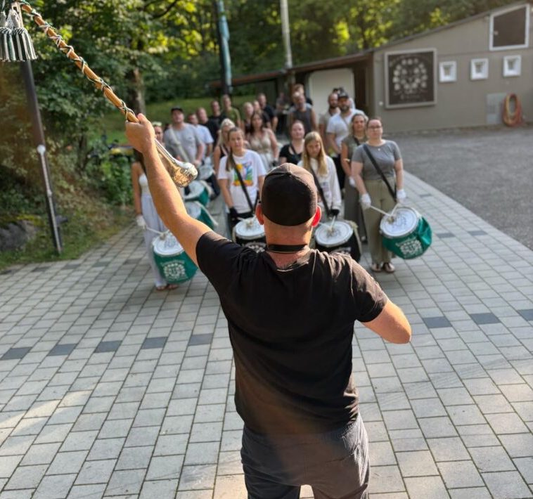 Eine Gruppe von Menschen, die in Reihen hinter einander stehen. Und vorne steht ein Mann