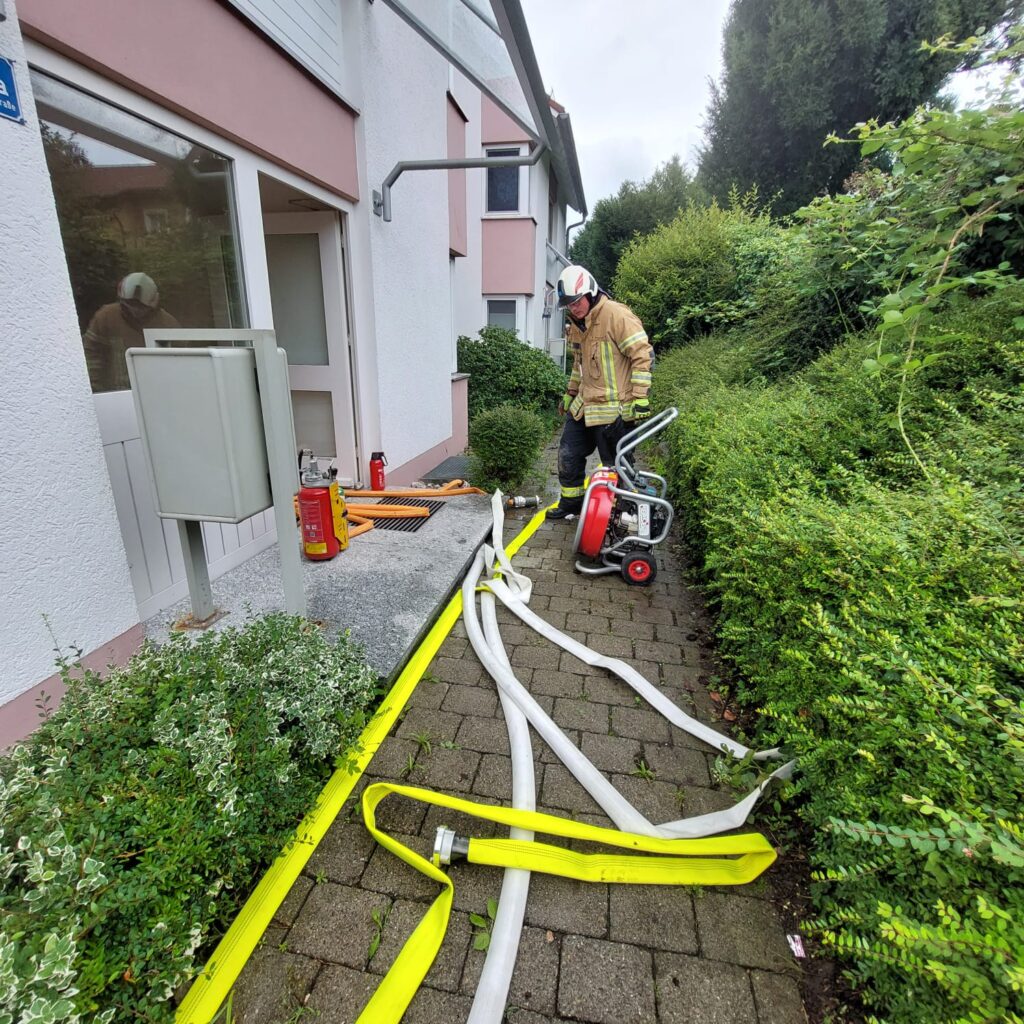 Ein Feuerwehrmann vor einem Haus mit Schläuchen.