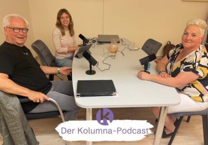 Drei Menschen sitzen an einem Tisch mit Mikros.