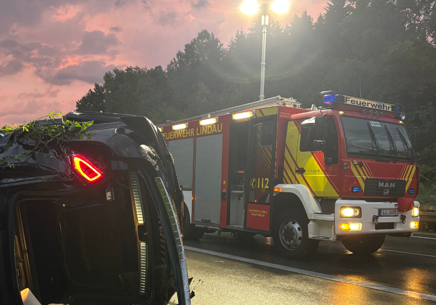 Zerstörtes Unfallauto abseits der rechten Autobahn-Fahrseite. Feuerwehrauto im Hintergrund.