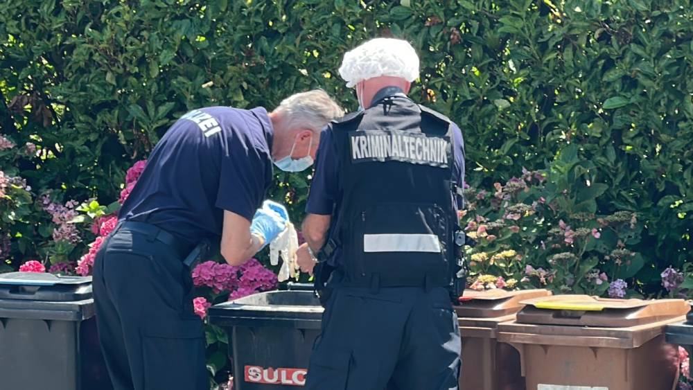 zwei Beamte der Kriminalpolizei durchsuchen Mülleimer.