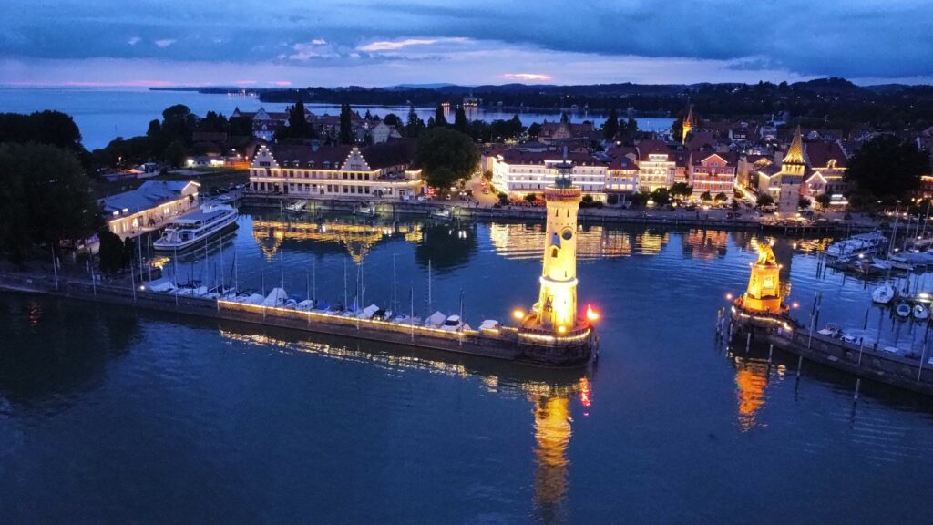 nächtlicher Blick von der Seeseite aus auf einen bedeuteten Hafen mit Turm und Häusern