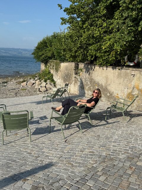 Eine Frau auf grünen Stühlen am Bodenseeufer.