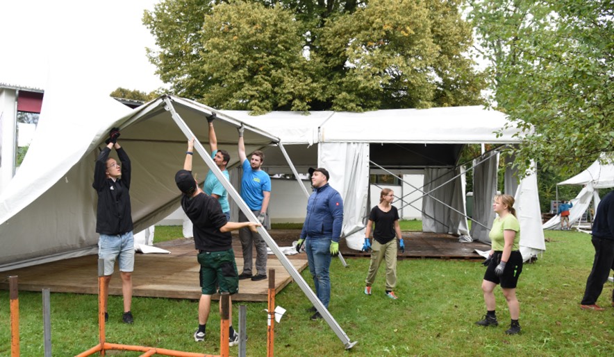 Mehrere Menschen bauen gemeinsam ein Zelt auf.