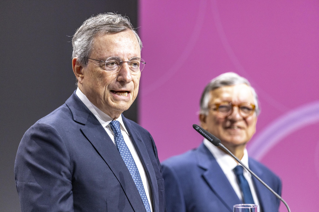 Ein Mann am Mikrofon und ein anderer Mann im Hintergrund.